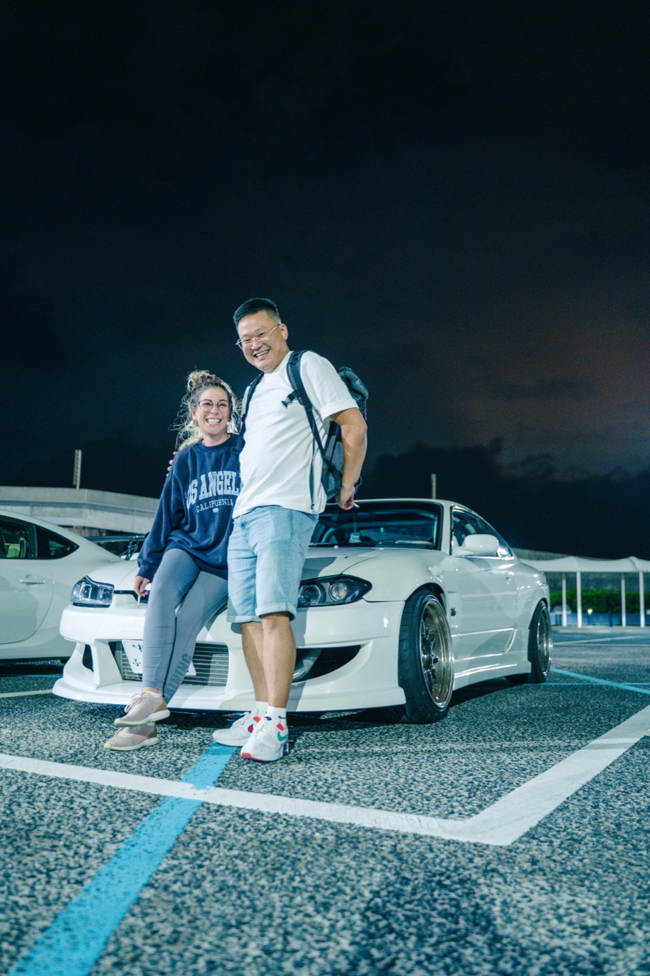 Guests with a white Nissan Silvia S15 at Daikoku PA — the van tour stops at the same spots